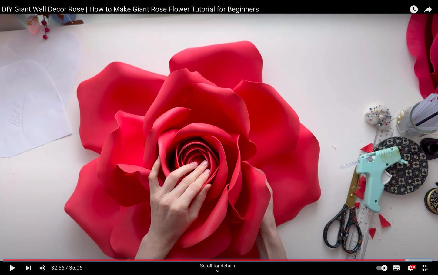 Red foam flower with a hand touching it, surrounded by crafting tools on a white surface.