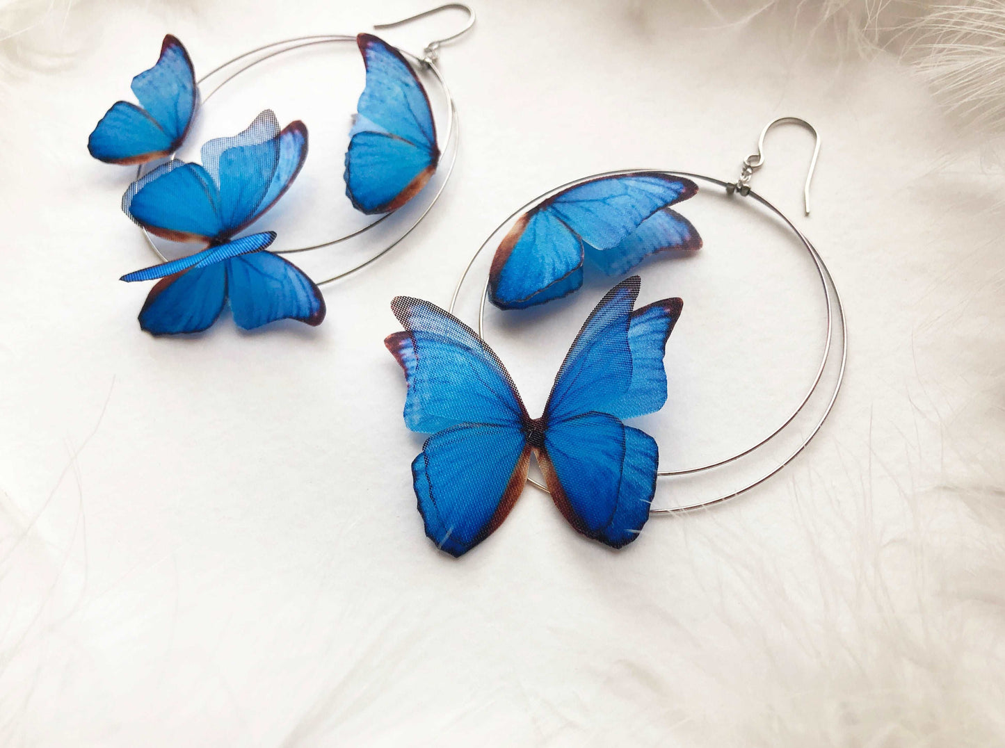 Silver Hoop Earrings with Blue Butterflies on White Feathers Background