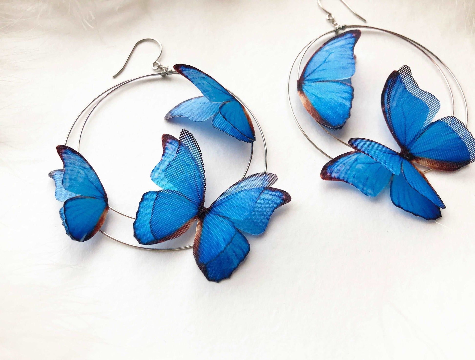 Silver Hoop Earrings with 3D Blue Butterflies on White Feathers Background