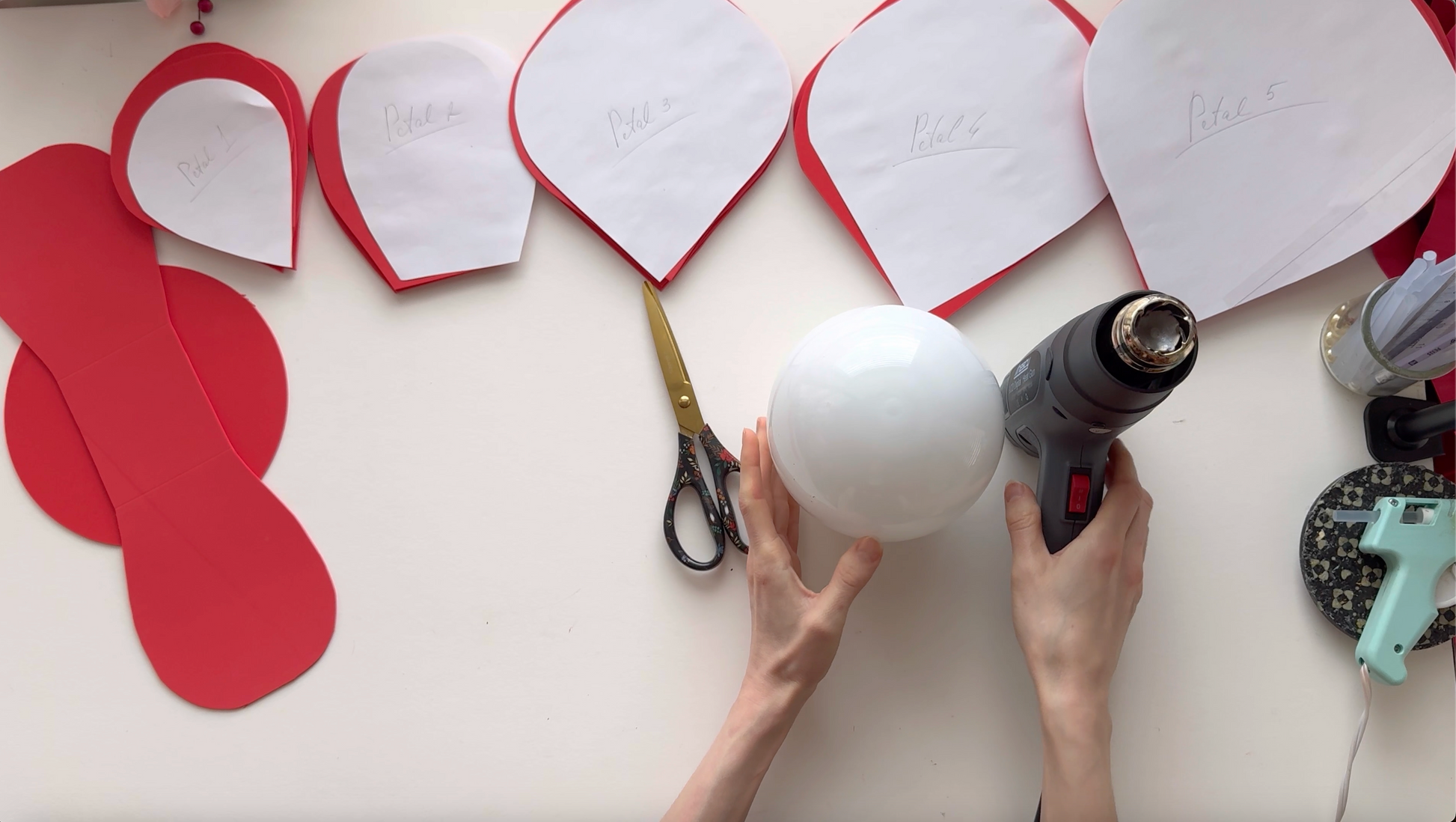 Alina Blossom using a hot glue gun to shape red petal-shaped cutouts on a white sphere and a white surface.