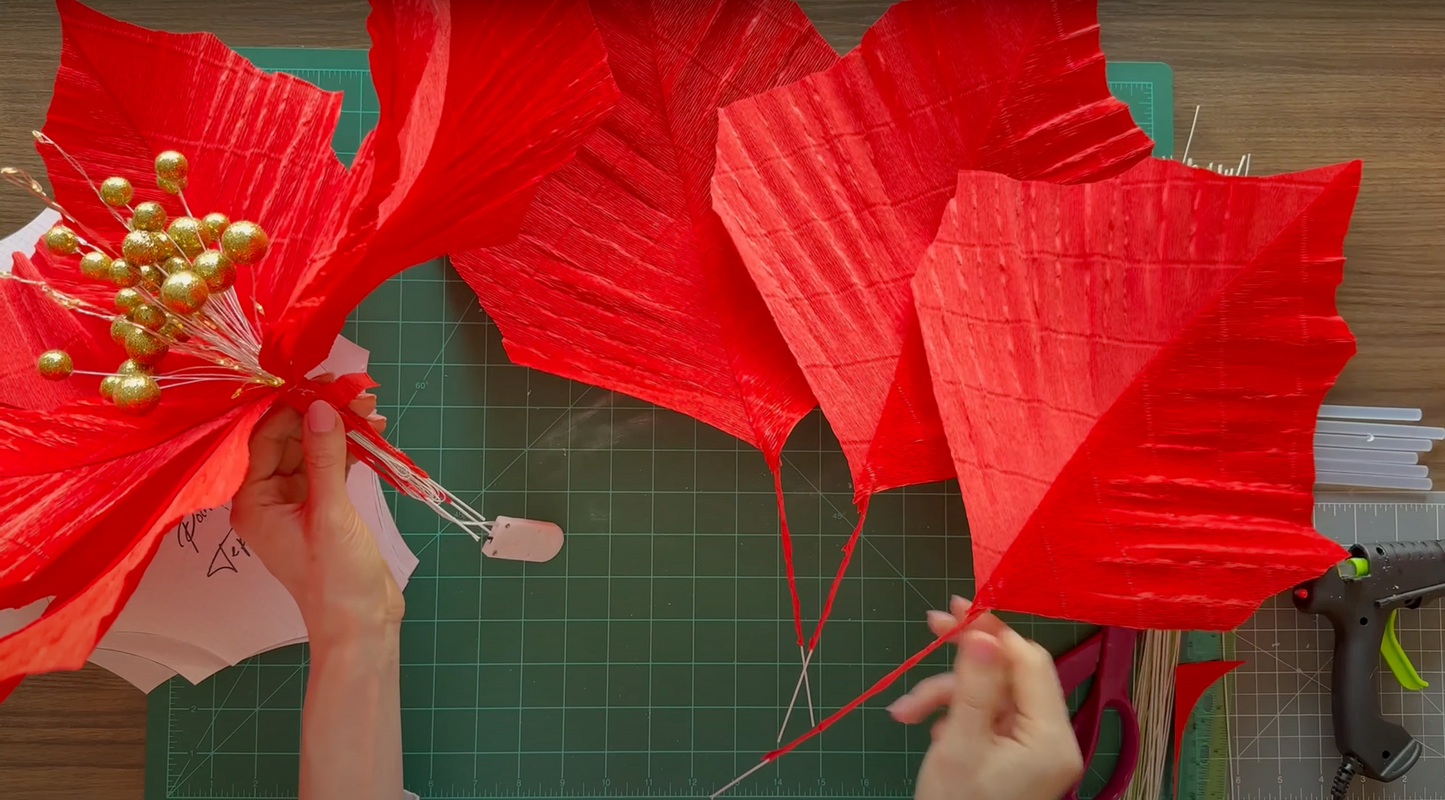 Giant Red Christmas Flower being crafted on a green cutting mat with a hot glue gun.
