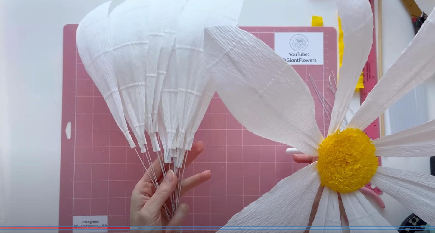 White paper flower with a yellow center held by hands on a pink cutting mat.