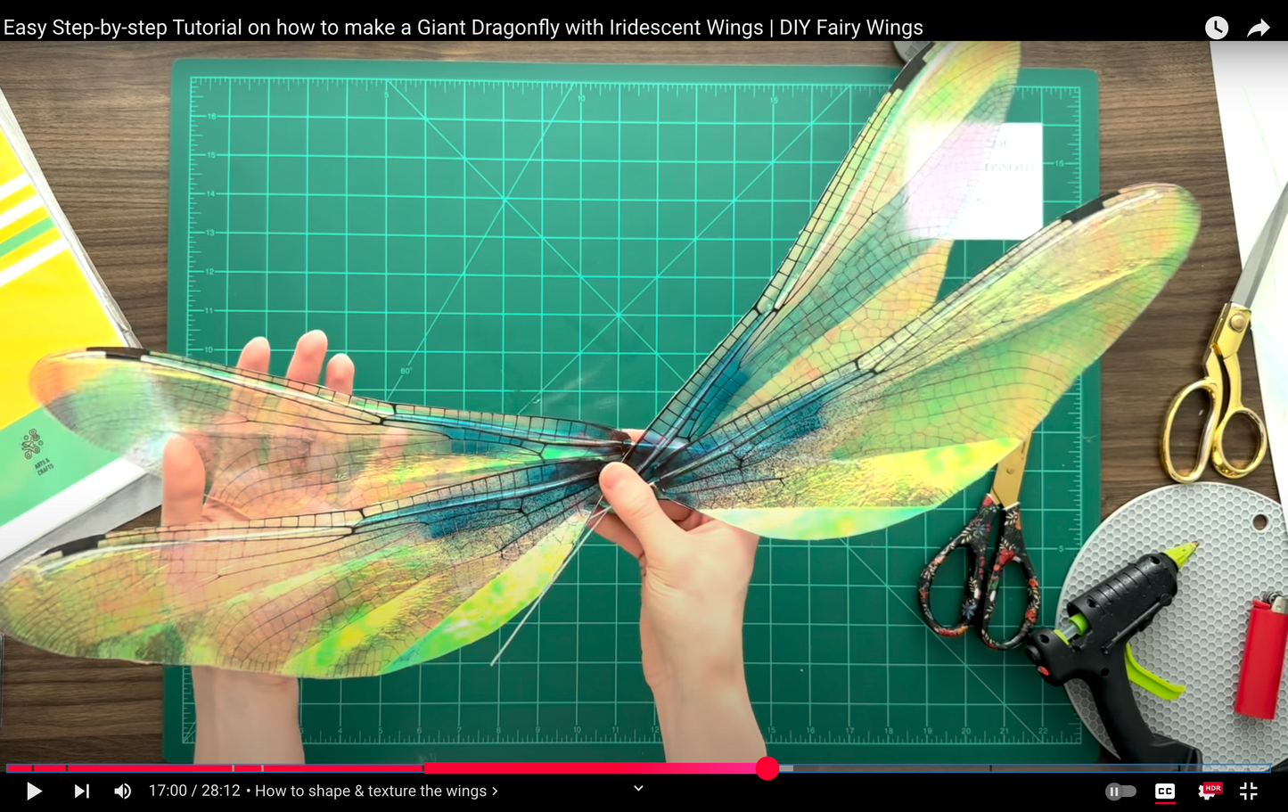 Person holding a large dragonfly model with iridescent wings on a cutting mat with crafting tools.