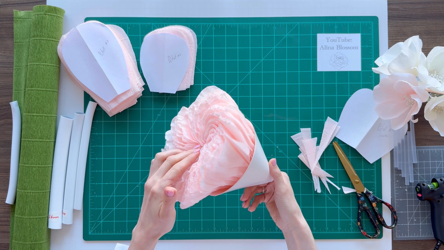 Hands working on a floral craft project with materials on a green cutting mat.