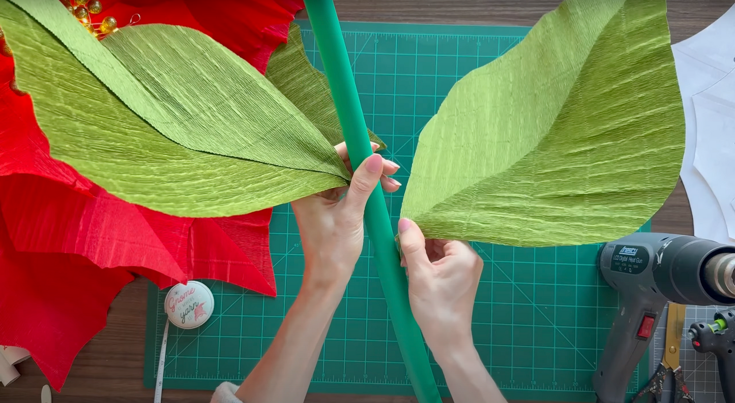 Alina Blossom holding a large green stem with paper leaves on a cutting mat.