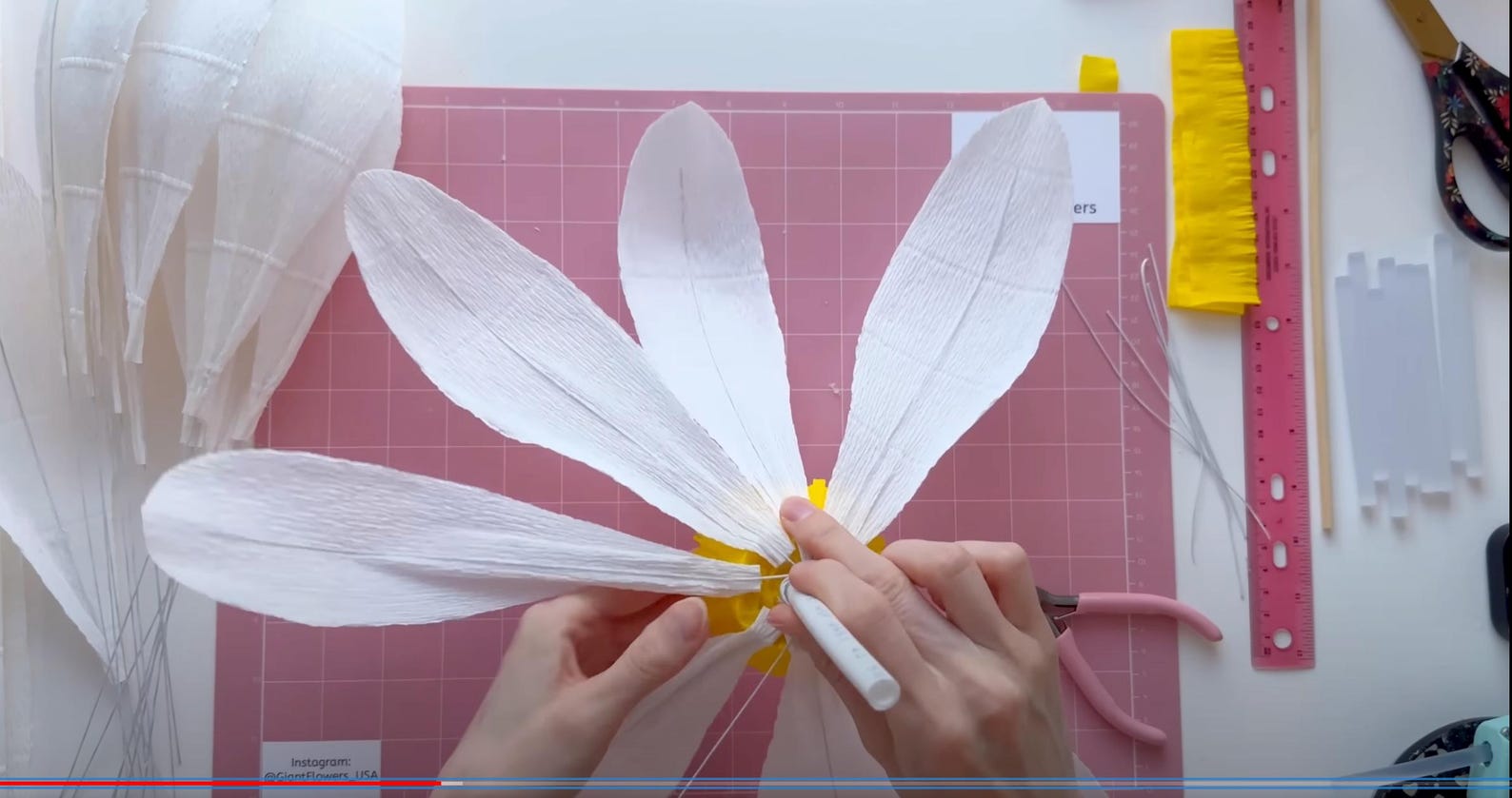 Alina Blossom assembling a Giant Daisy paper flower on a pink cutting mat with tools in the background