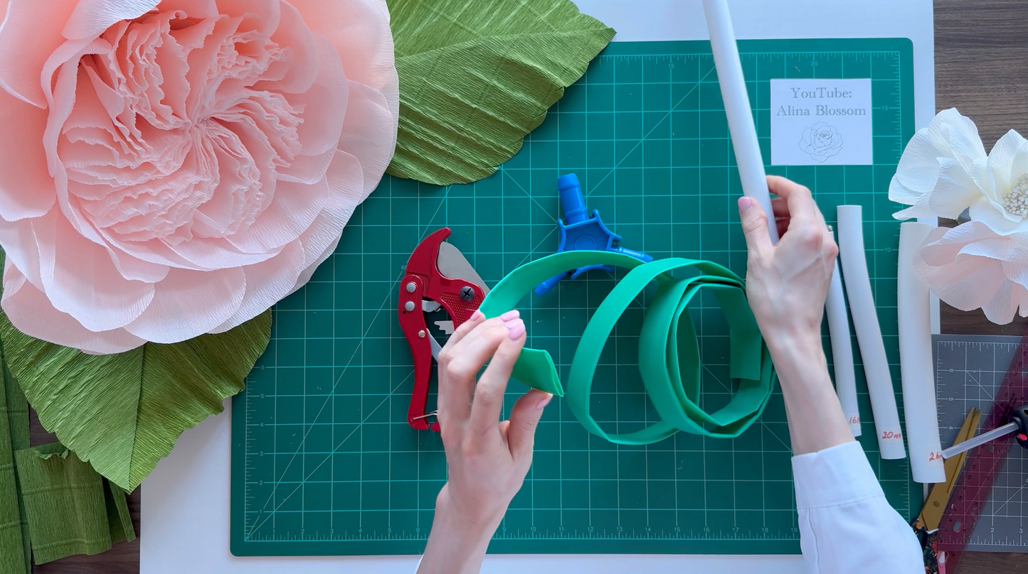 Person crafting paper flowers on a green cutting mat with tools.