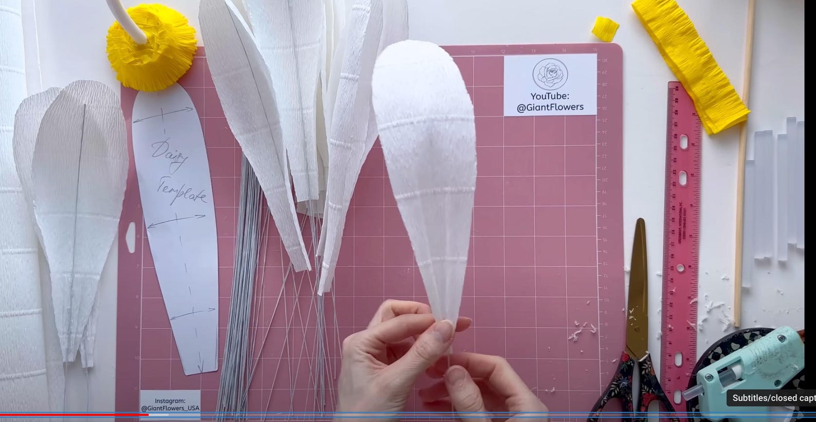 Hand crafting paper flowers on a pink cutting mat with tools and templates.