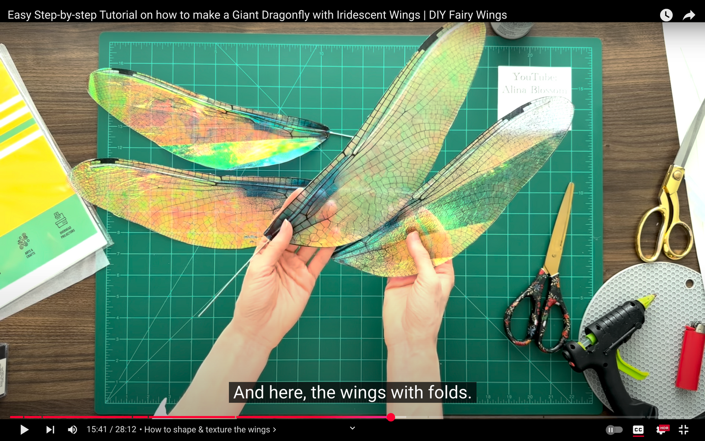 DIY fairy wings with iridescent colors on a green cutting mat with tools.