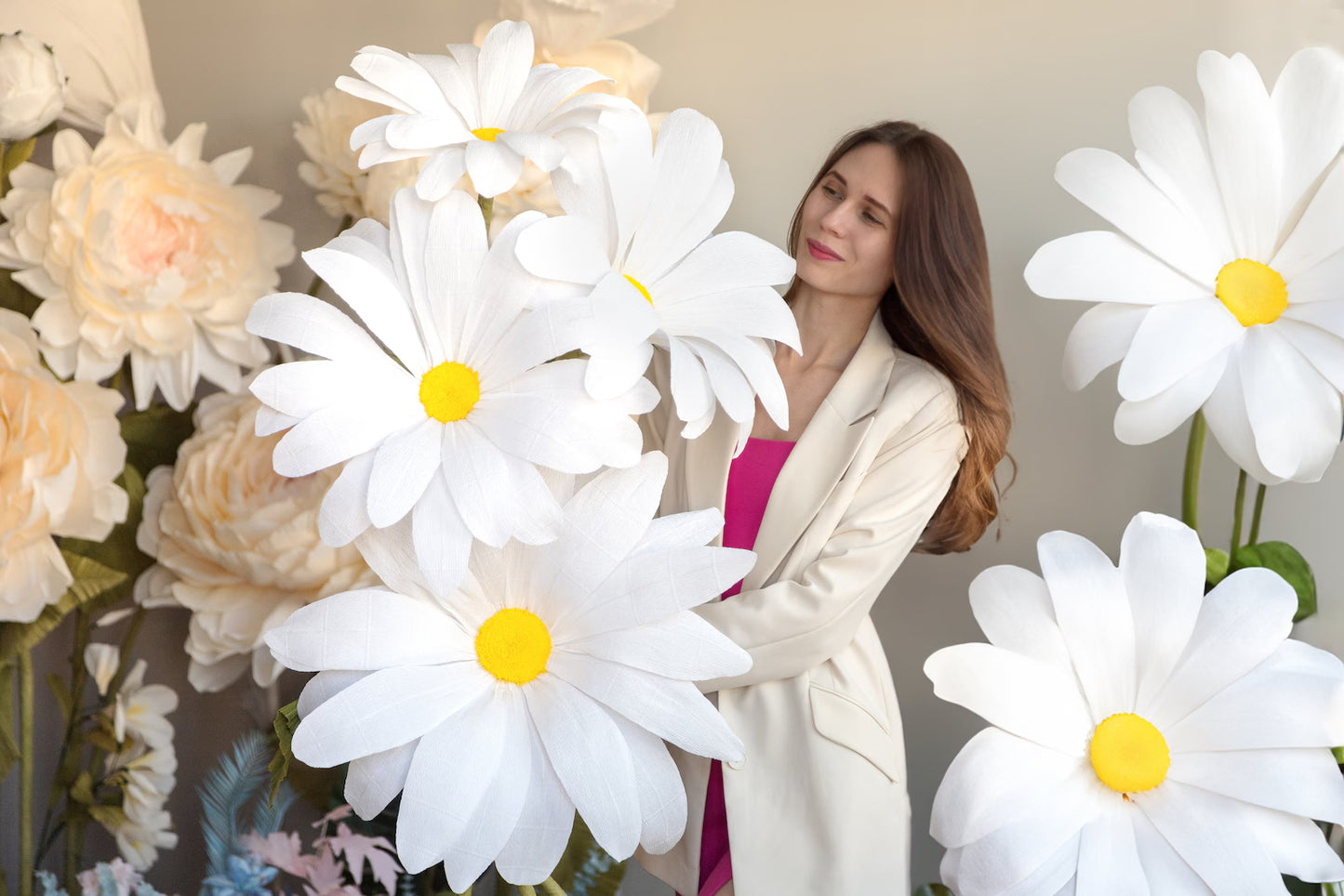 Alina Blossom standing among Giant Daisy flowers with yellow centers, wearing a white jacket.