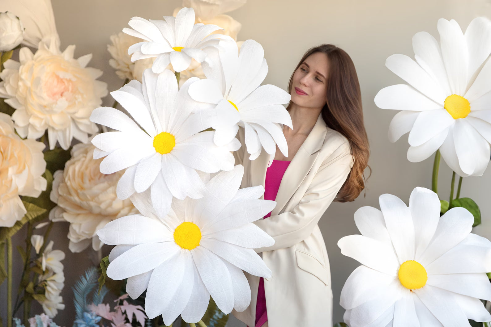 Alina Blossom standing among Giant Daisy flowers with yellow centers, wearing a white jacket.