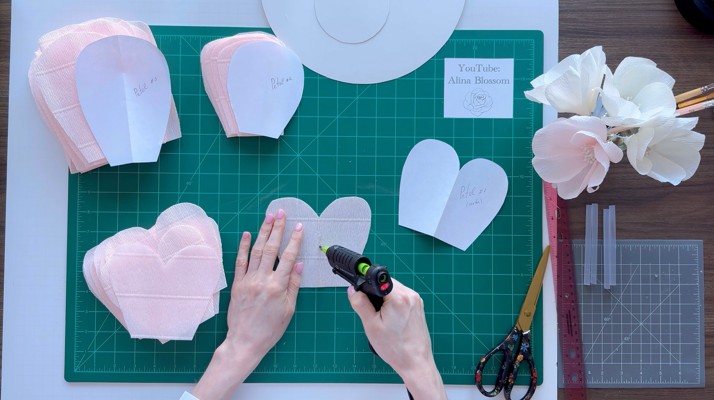 Alina Blossom crafting paper heart shapes on a green cutting mat with tools and flowers.