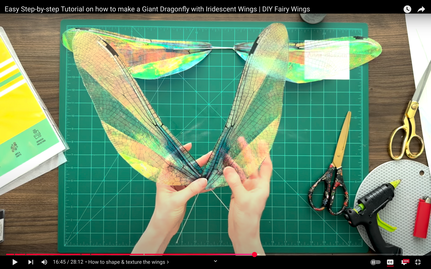 DIY tutorial on making iridescent fairy wings with hands holding the wings on a cutting mat.