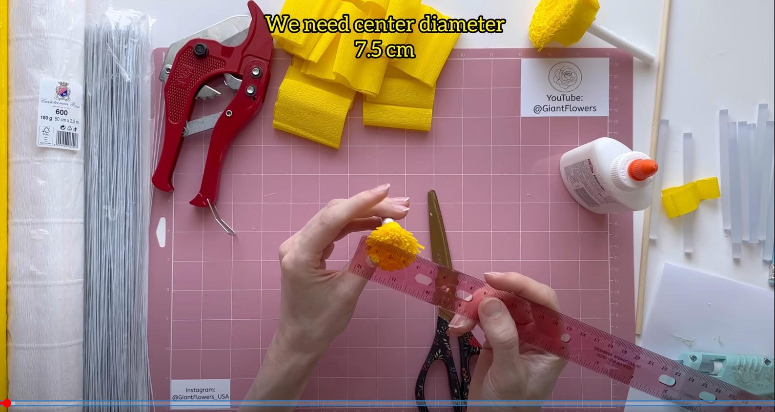 Person measuring yellow flower center diameter with a ruler on a pink cutting mat.