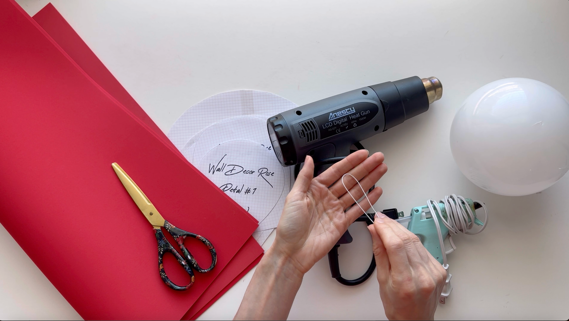 Hot glue gun, scissors, red foam, and a white sphere on a white surface.