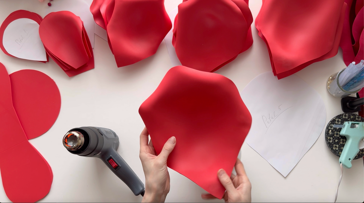 Red paper flower petals being shaped with a hot glue gun on a white surface.