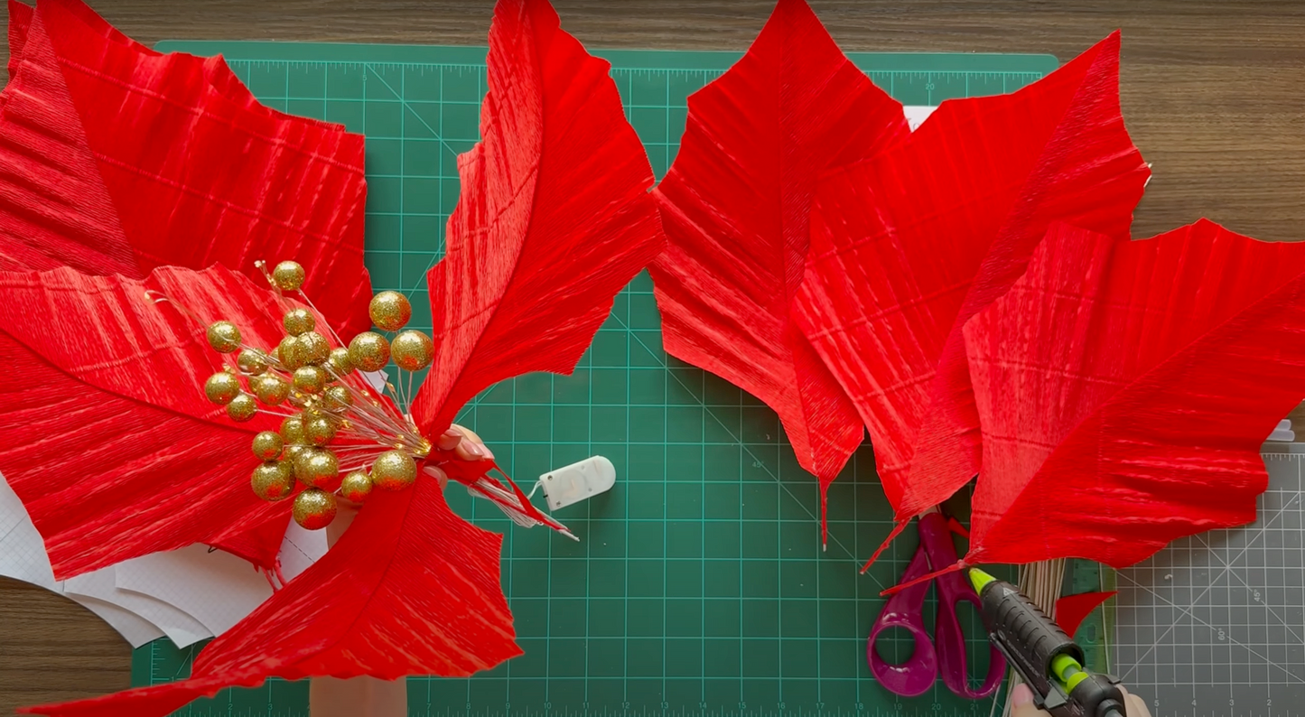 Red Christmas flower with petals and gold accents on a green cutting mat.
