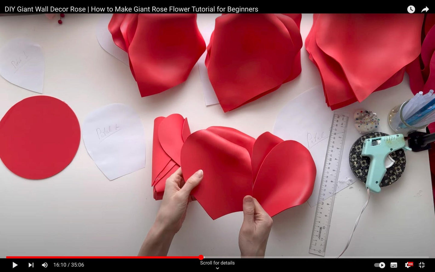 Hands working with red paper to create a giant rose flower on a white surface.