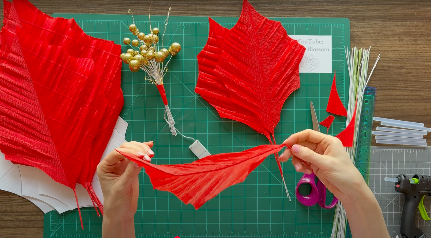 Alina Blossom tutorial for Giant Christmas Flower: crafting red paper leaves on a green cutting mat with scissors and other materials.