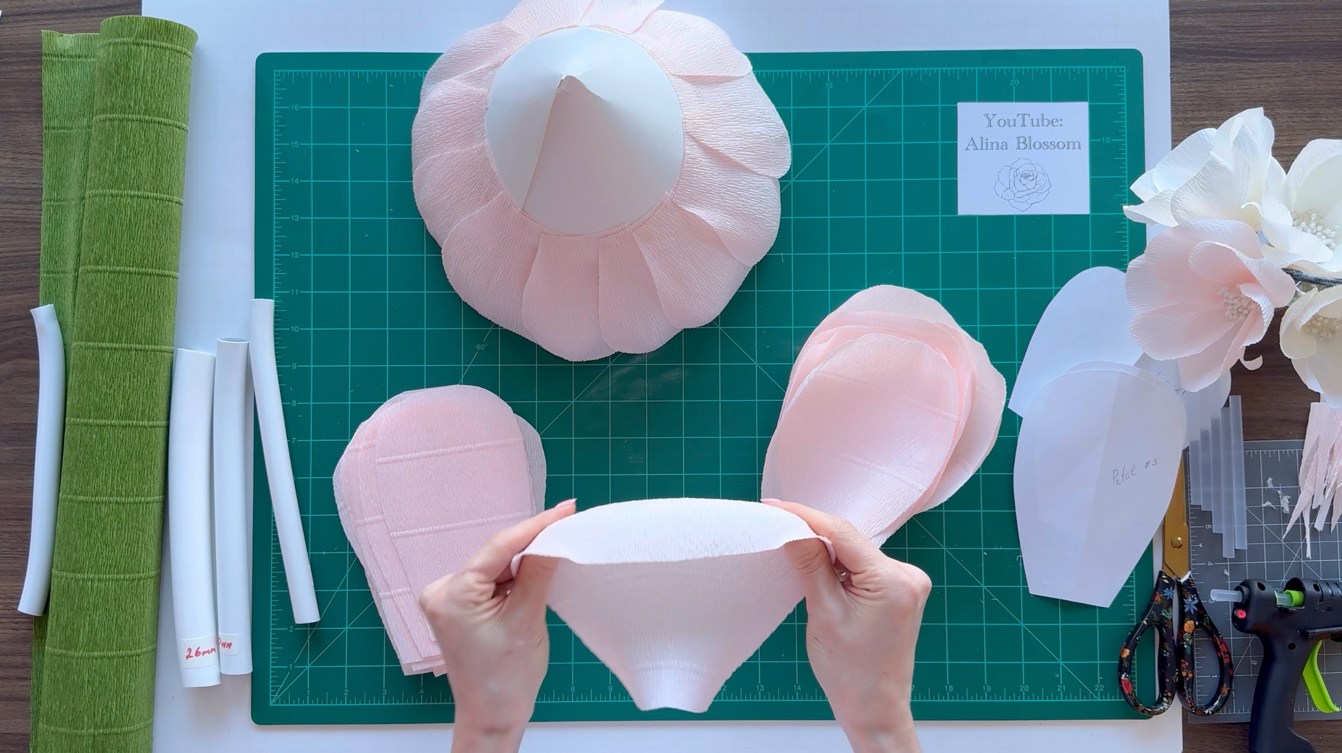 Hands working with paper flower templates on a cutting mat.