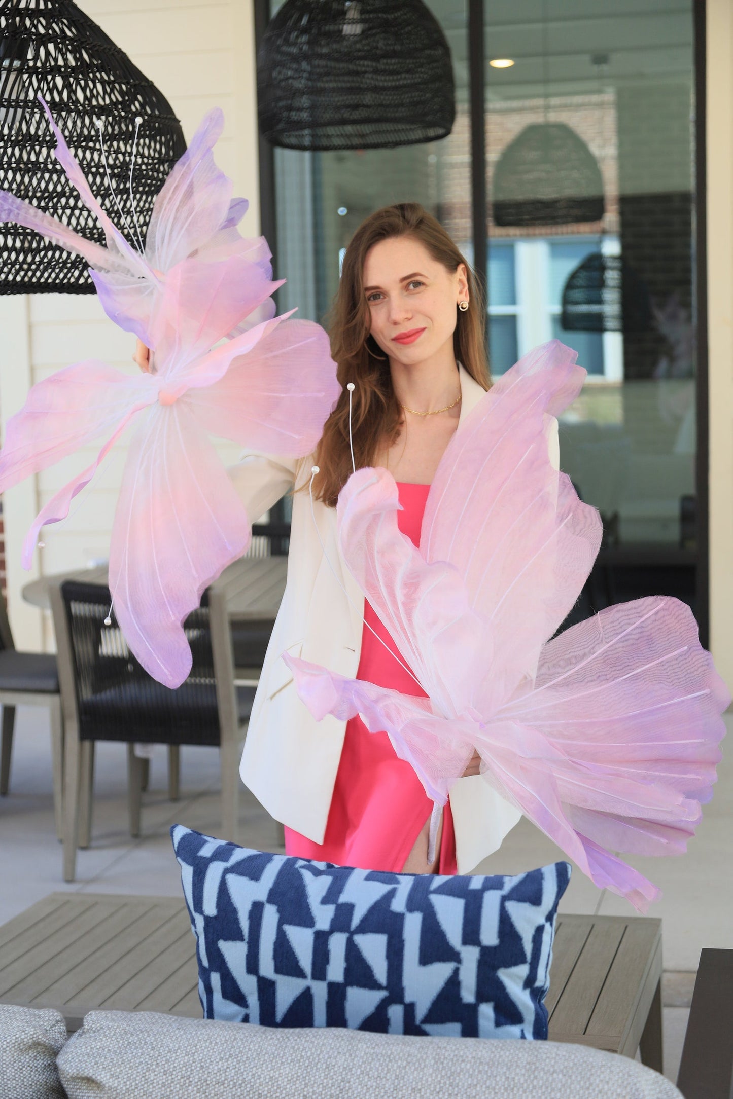 Woman holding pink floral props in an outdoor setting with a blue patterned pillow on a table.