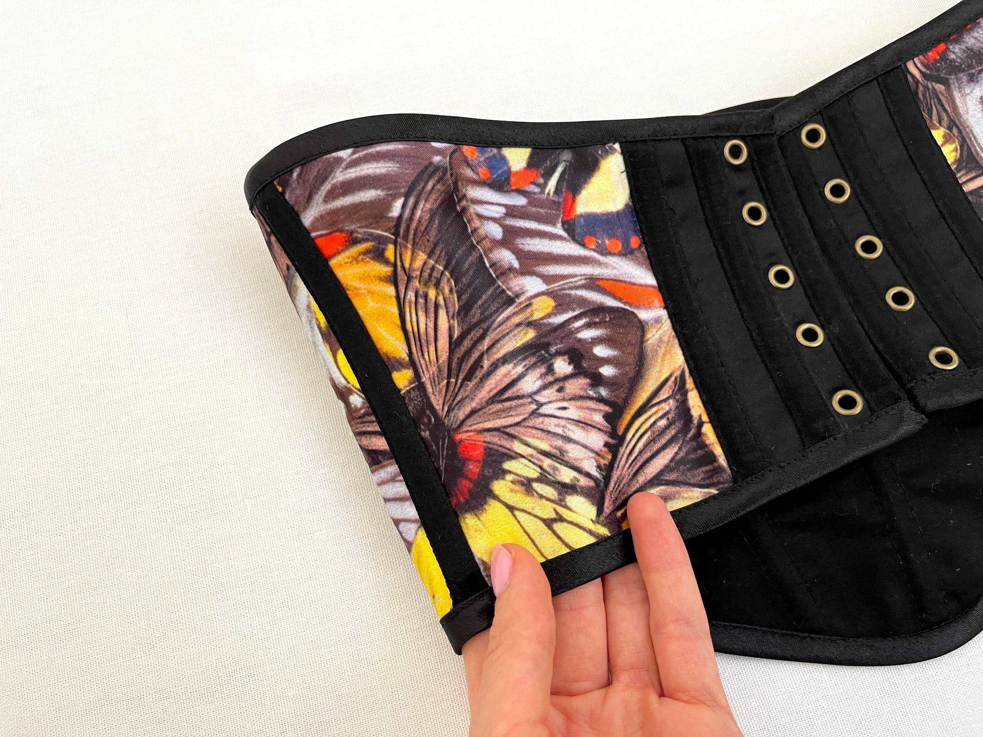 Hand holds black corset with yellow butterfly canvas on white background